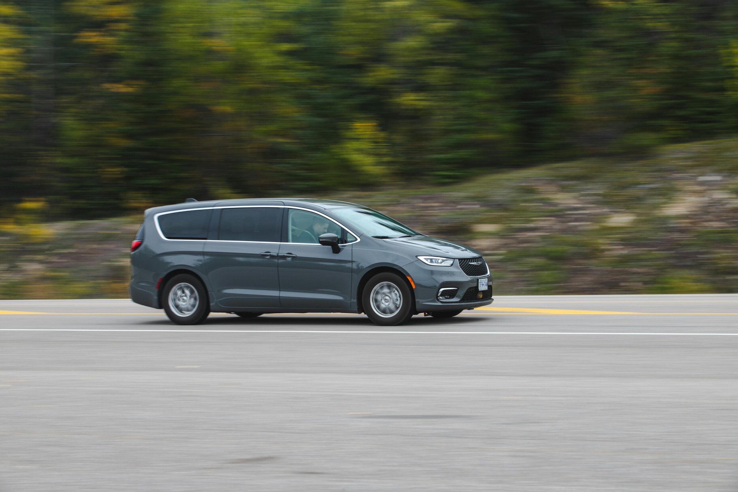 A modern minivan moving swiftly on a scenic highway surrounded by lush greenery.