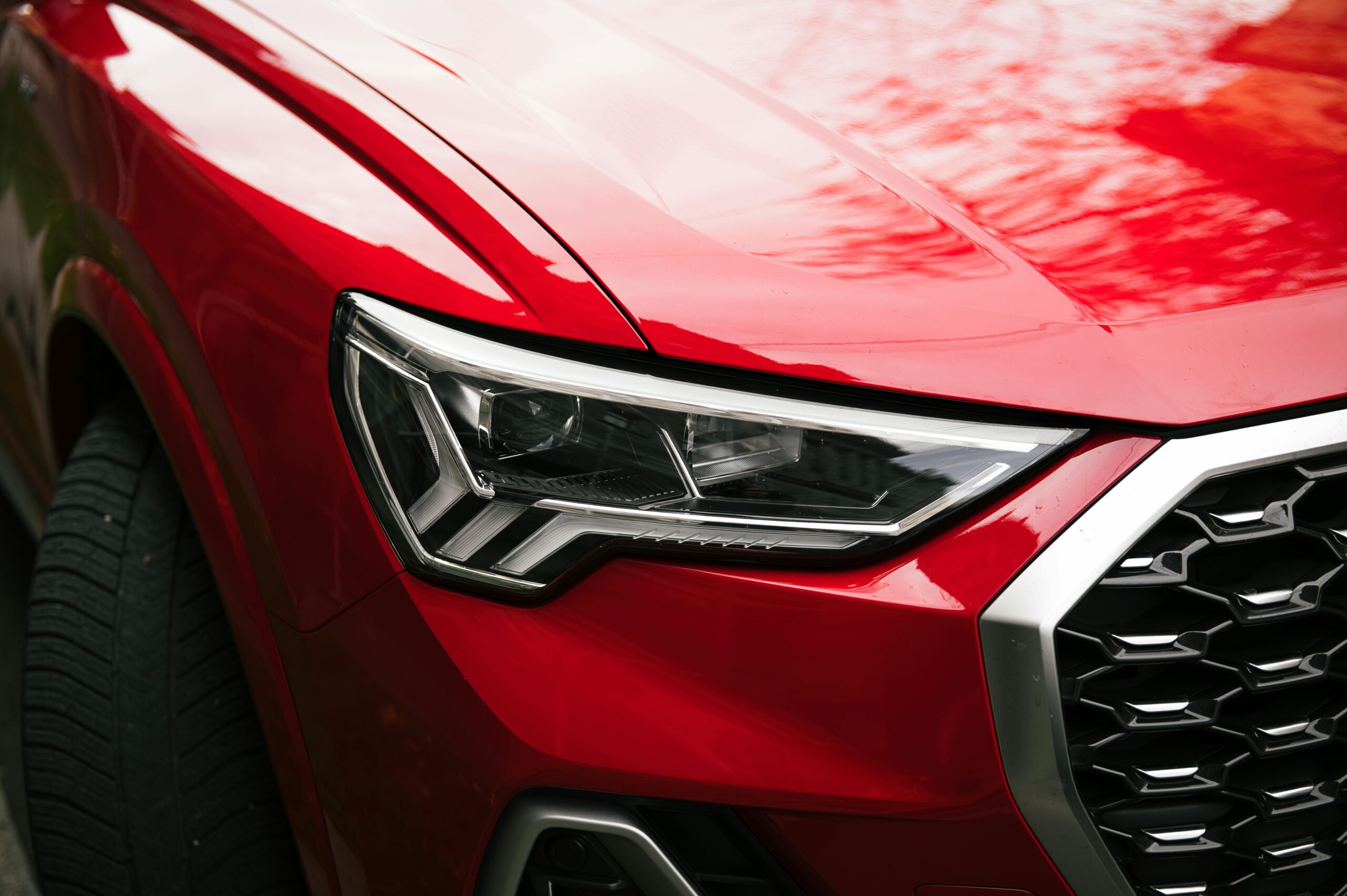 Detailed view of a red car's sleek headlight and grille design outdoors.